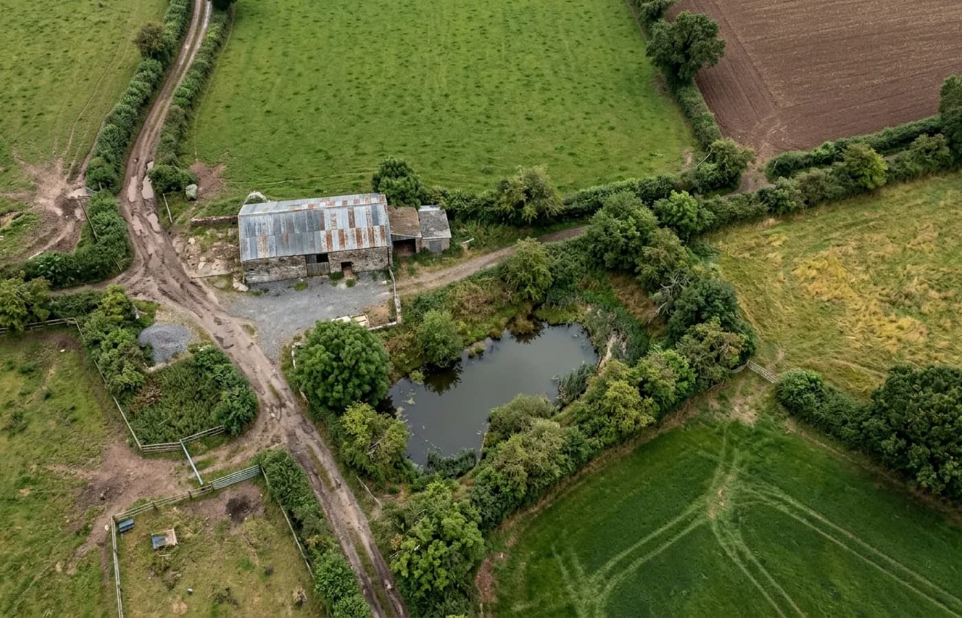Aerial view looking straight down over Devon farmland showing hedged field boundaries, a farm track, a pond and a stone barn with a corrugated roof